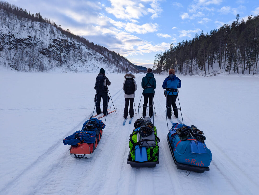 Women on backcountry skis pulling sleds through snowy forest on a ski expedition