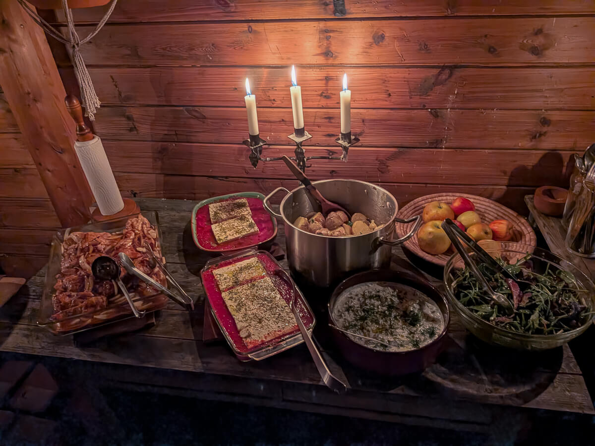 Women’s winter camping food prep on a stove inside a wooden cabin in Sweden, with candles lit