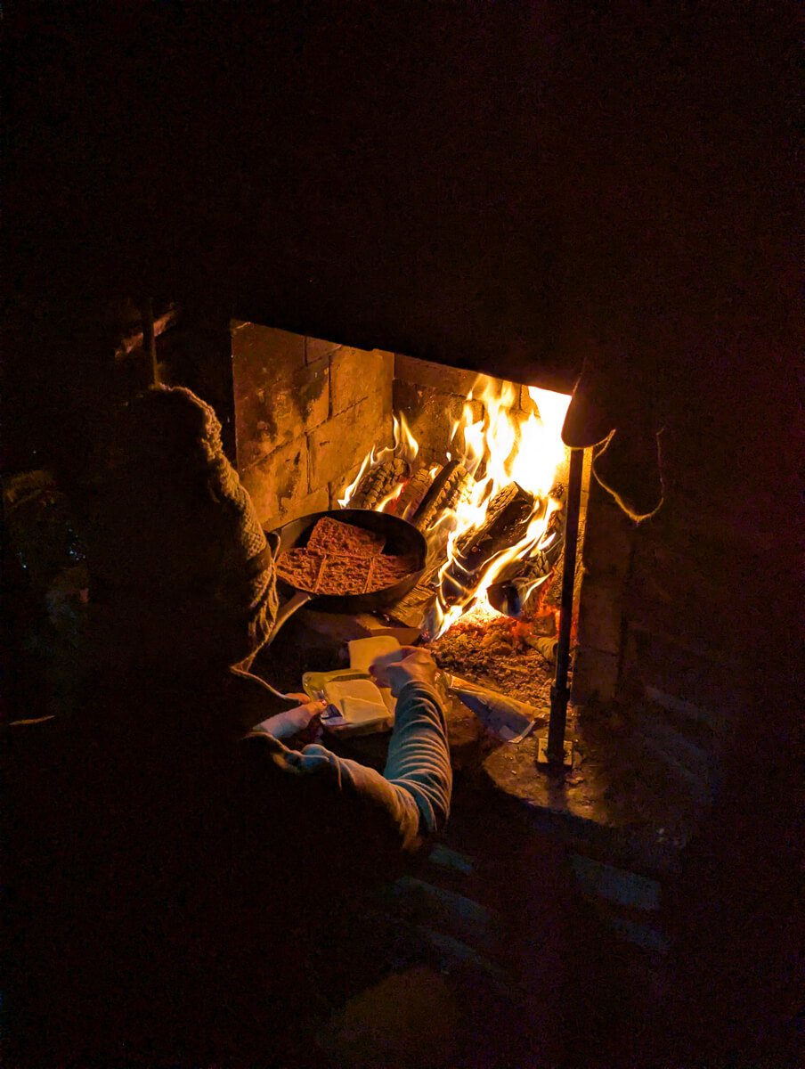 Fire burning inside a backcountry hut at night, with people warming by the stove