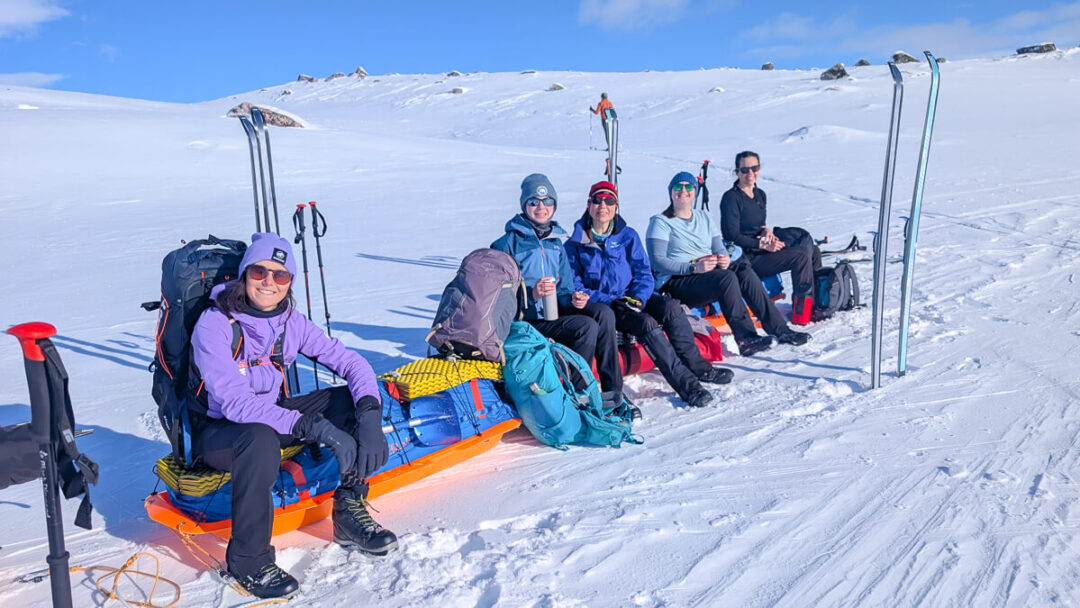 Women on skis posing on snowy mountain slope with ski poles and backpacks during a backcountry ski trip