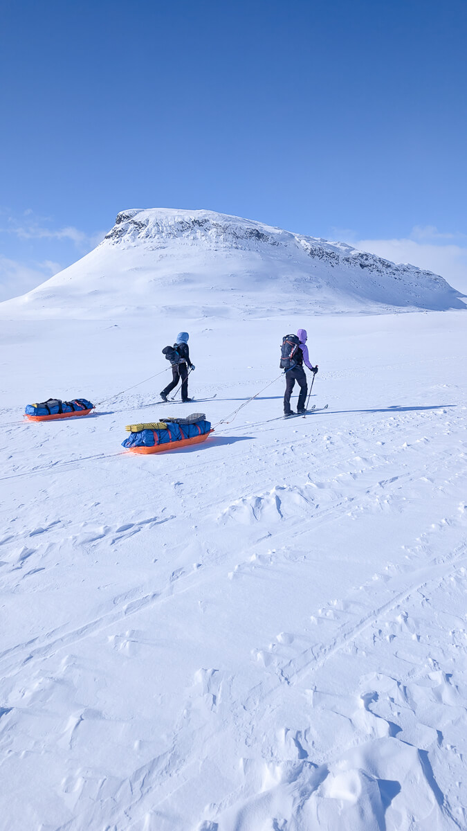Women backcountry skiing across snowy mountains, pulling sleds on a hut-to-hut route