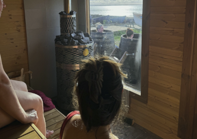 Woman in a wooden sauna with steam from the stove heater, looking through a glass window