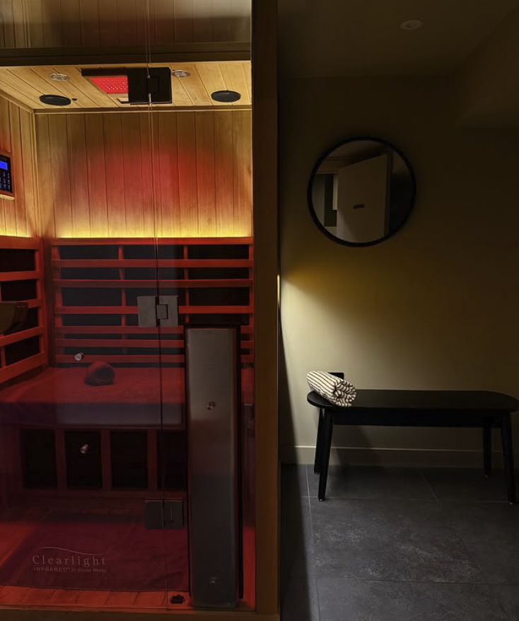 ClearLight infrared sauna with red lighting and glass door, next to a small bench in a UK spa room