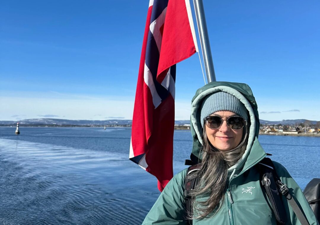 Woman on the Oslo waterfront beside a Norwegian flag in clear winter daylight