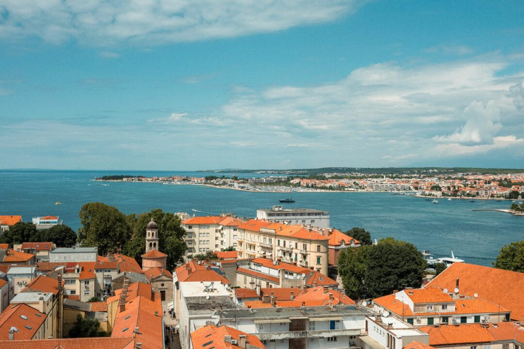 Woman stands overlooking orange-roofed old town and Adriatic sea in Zadar, Croatia