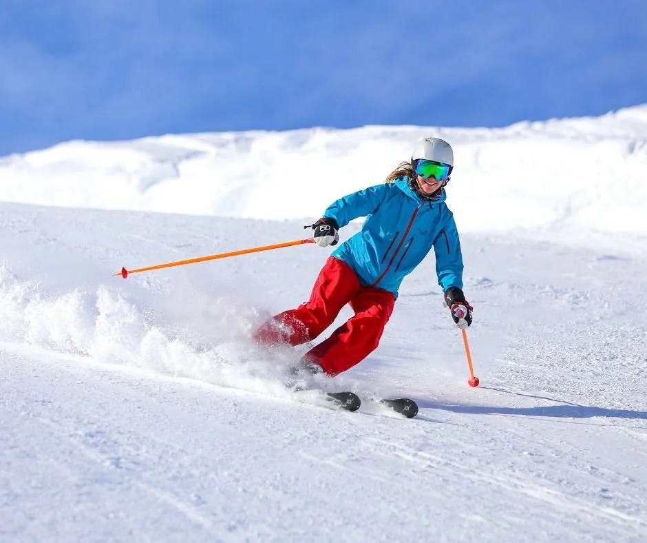 Women alpine skiing on a snowy slope, carving turns with goggles and helmet under blue sky