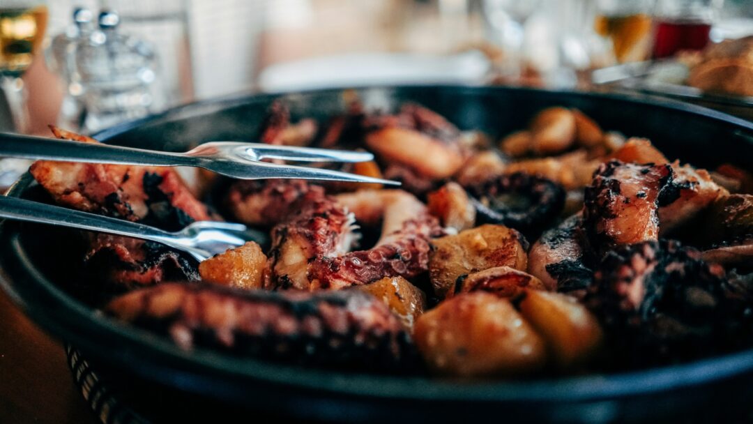 Grilled meat in a black pan, served with tongs in a restaurant setting