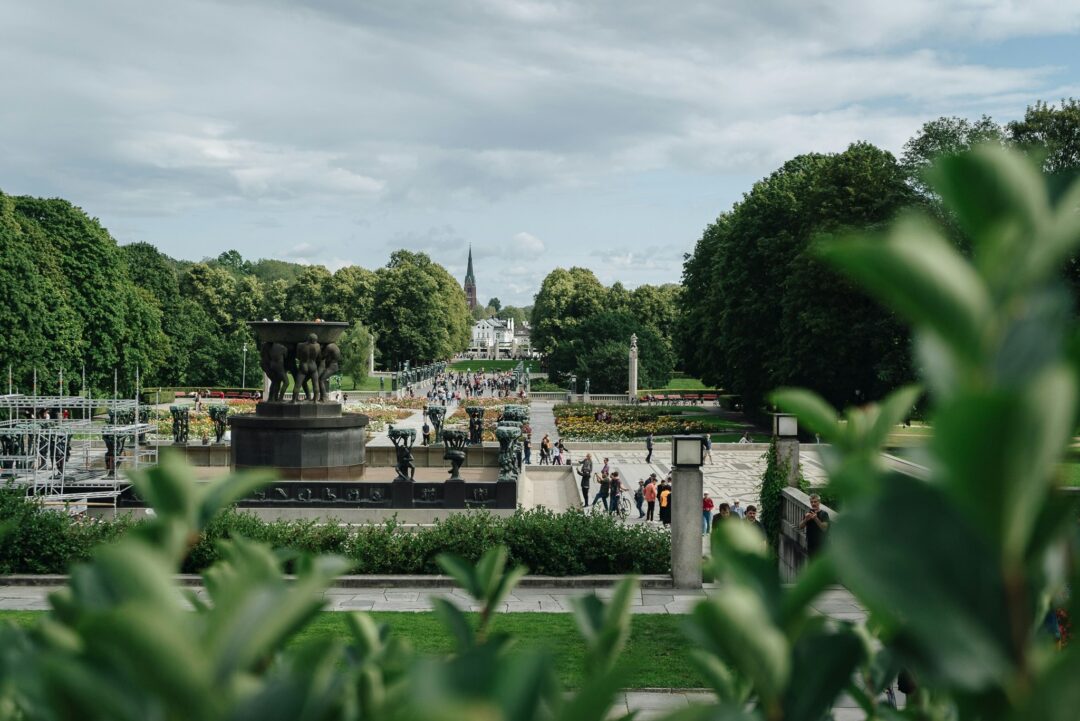 Women’s city stroll through Oslo gardens and fountains, with a church spire in the distance