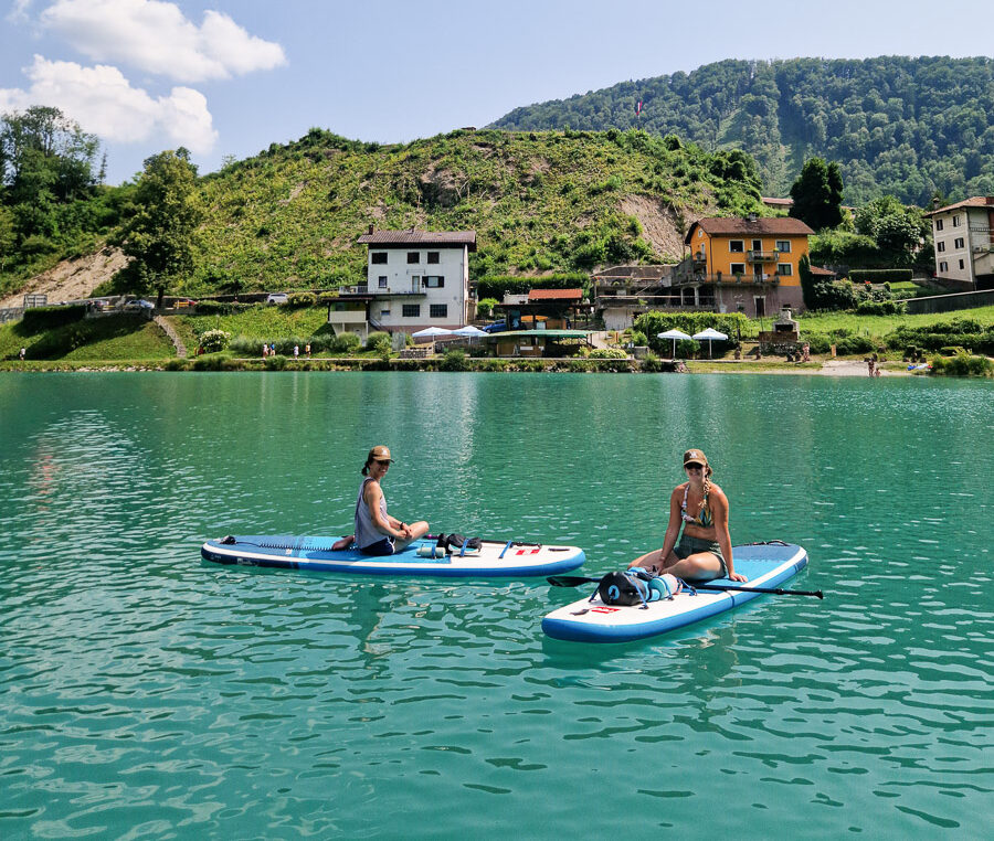 Two women on stand-up paddleboards on a green lake in a Slovenian village.