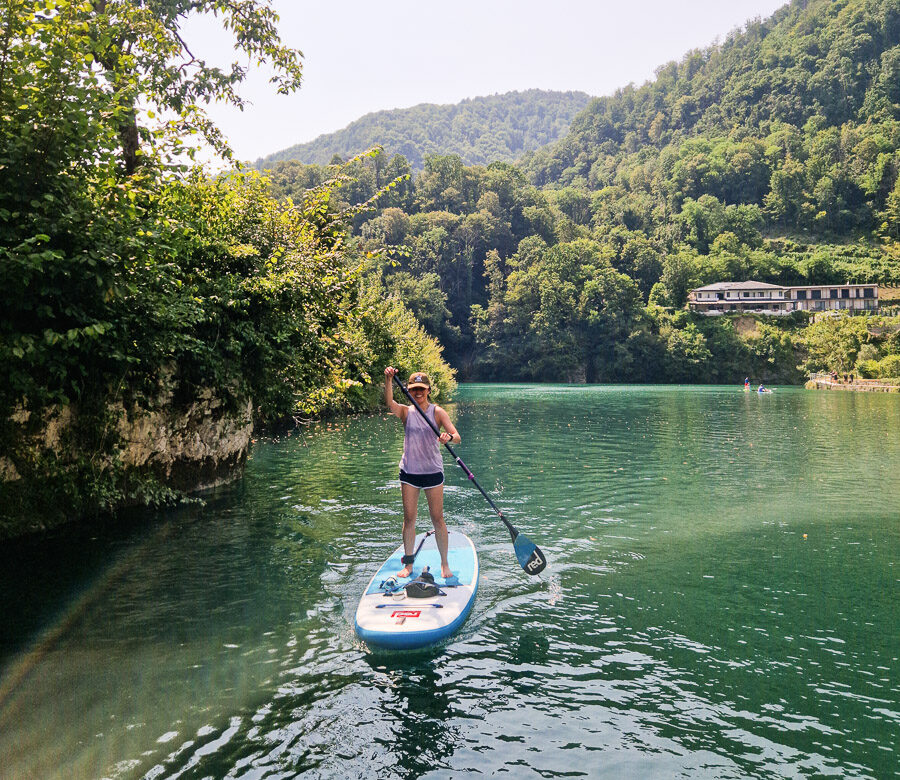 Woman stand-up paddleboarding on a calm river in Slovenia, surrounded by forested hills