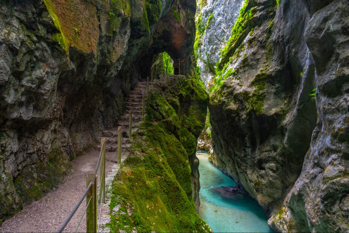 Turquoise river in a narrow gorge with a riverside walkway and railings, surrounded by steep green cliffs