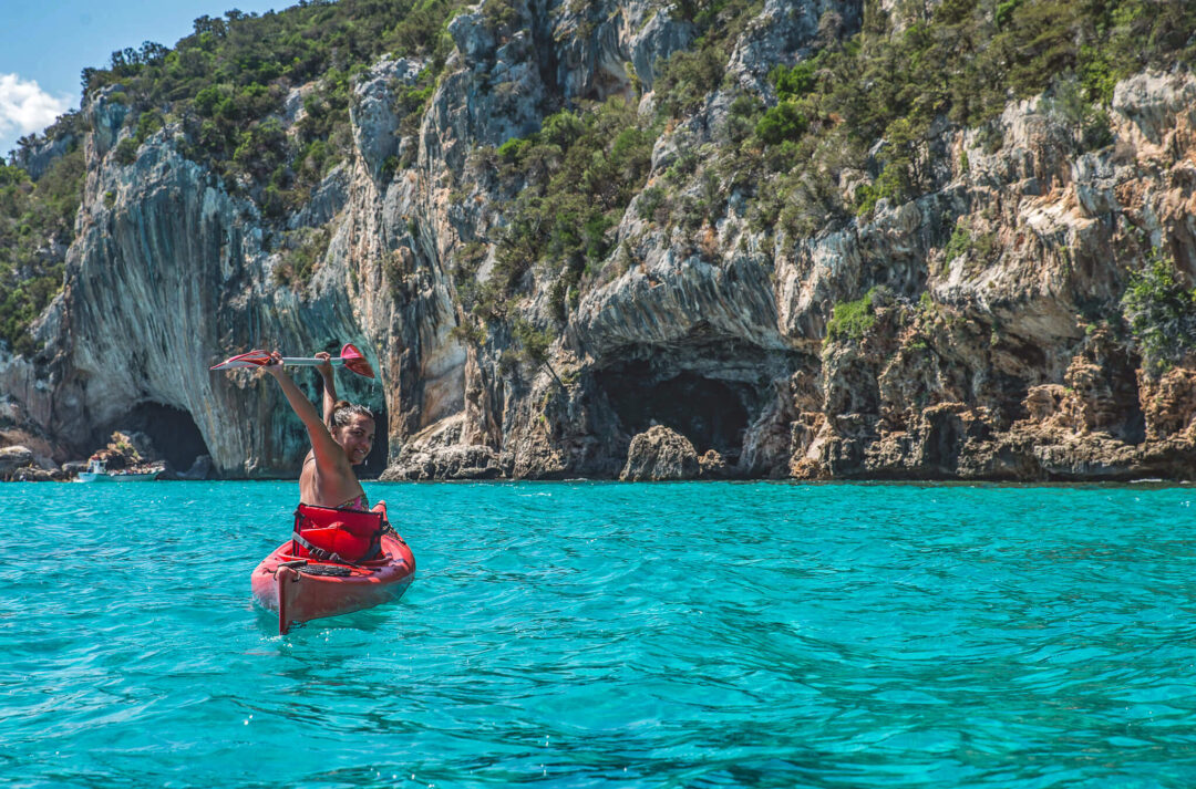 Woman kayaking in calm turquoise sea beside rocky coastal cliffs