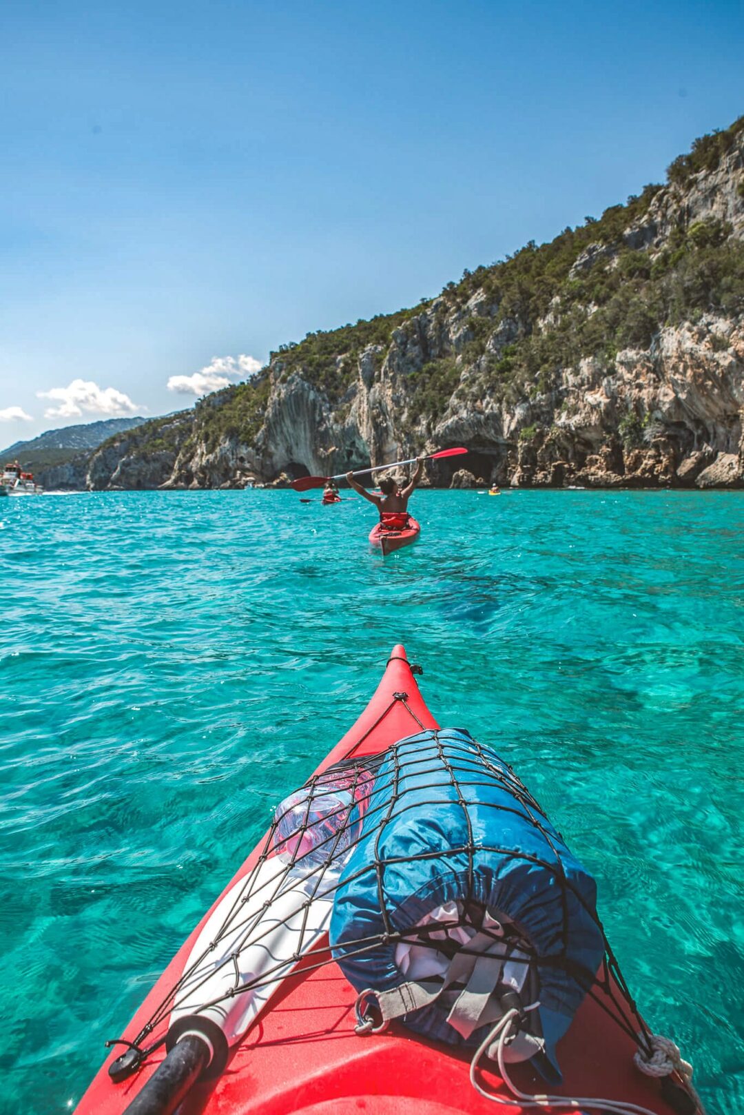 Woman kayaking on turquoise sea near a rocky coastline