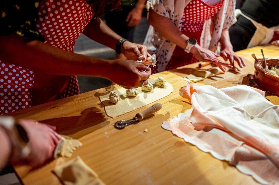 Women in polka-dot aprons prepare food together at a wooden table, hands shaping and topping pastries