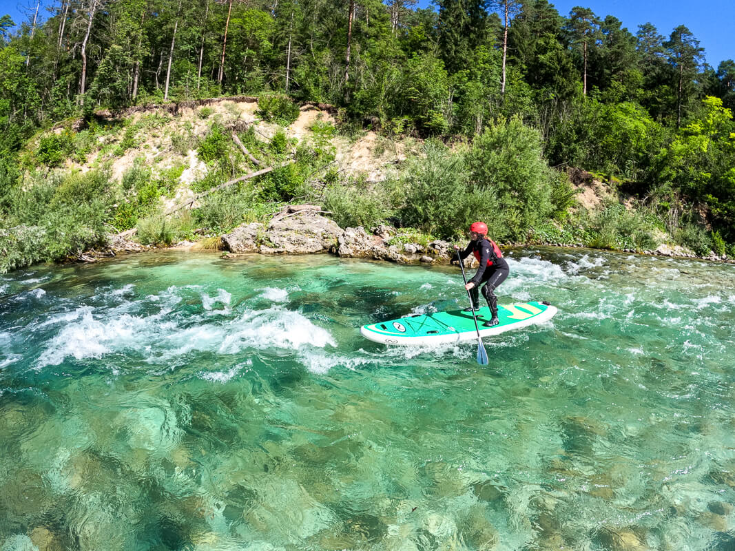 Woman SUP paddleboarding on whitewater rapids in a clear forest river