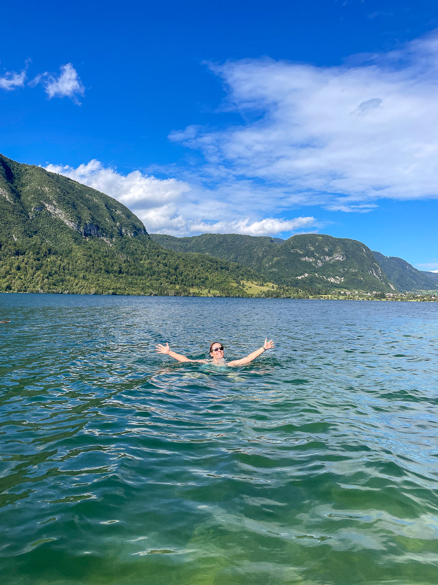 Woman stand-up paddleboarding on a calm mountain lake with forested peaks under a blue sky