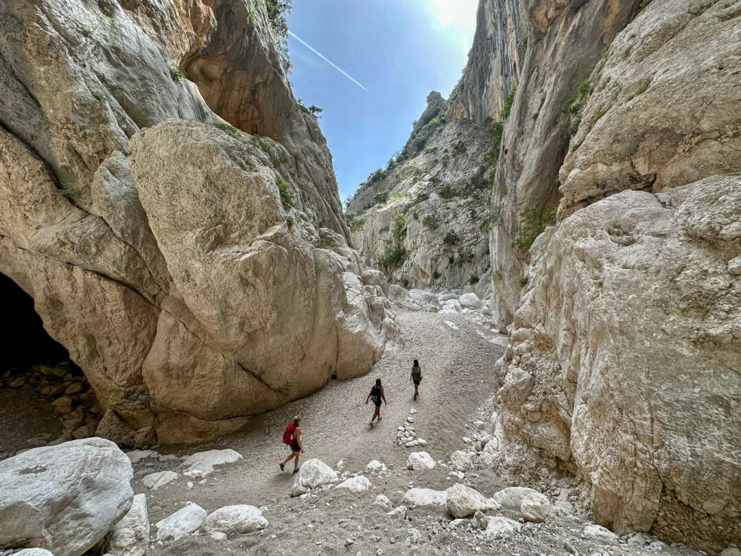 Hikers walking along a narrow rocky gorge with a stream in the background