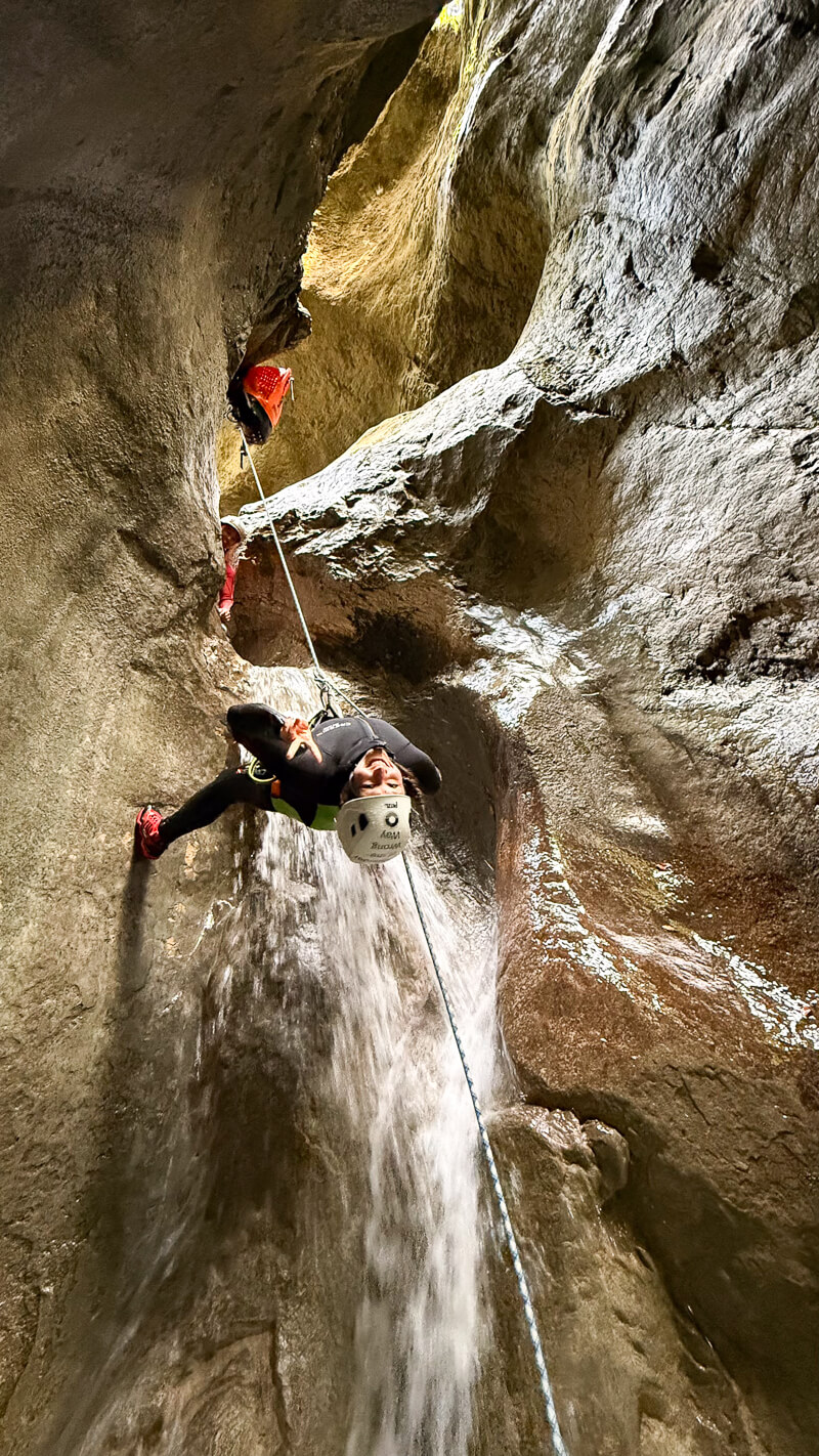 Woman canyoning through a narrow rocky gorge with a rope and flowing waterfall in Slovenia