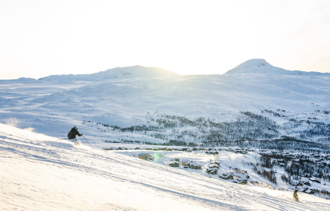 Downhill skier on a snowy slope with Norwegian mountains and ski village below in winter landscape