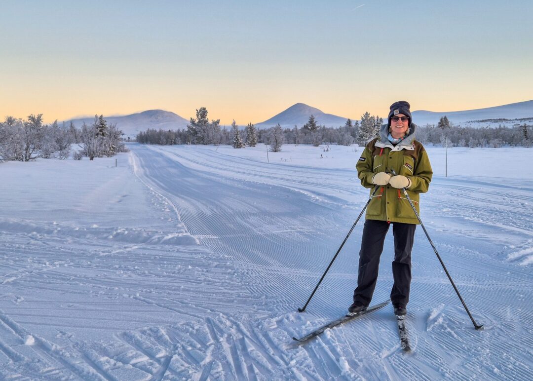 Women cross country skiing on a snowy trail in the mountains at sunrise, with skis and poles.