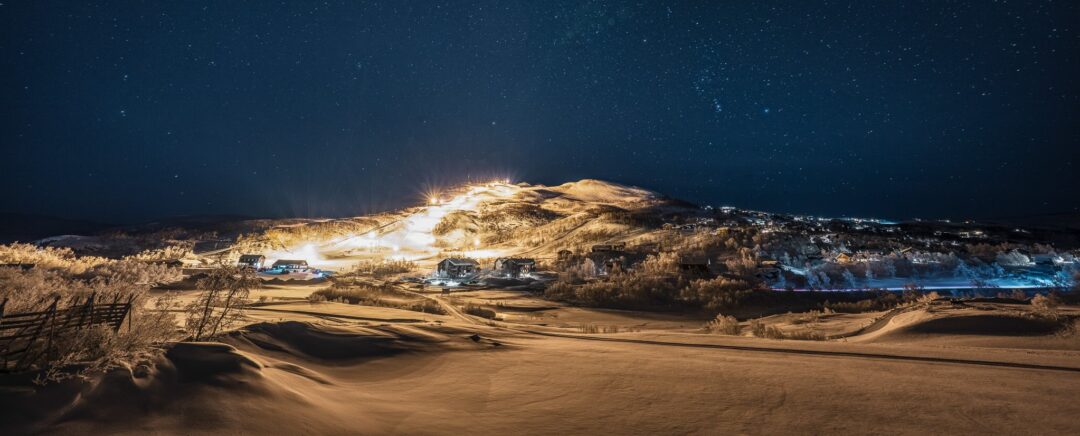 Snowy downhill ski slopes at night under a starry sky with illuminated pistes and hillsides