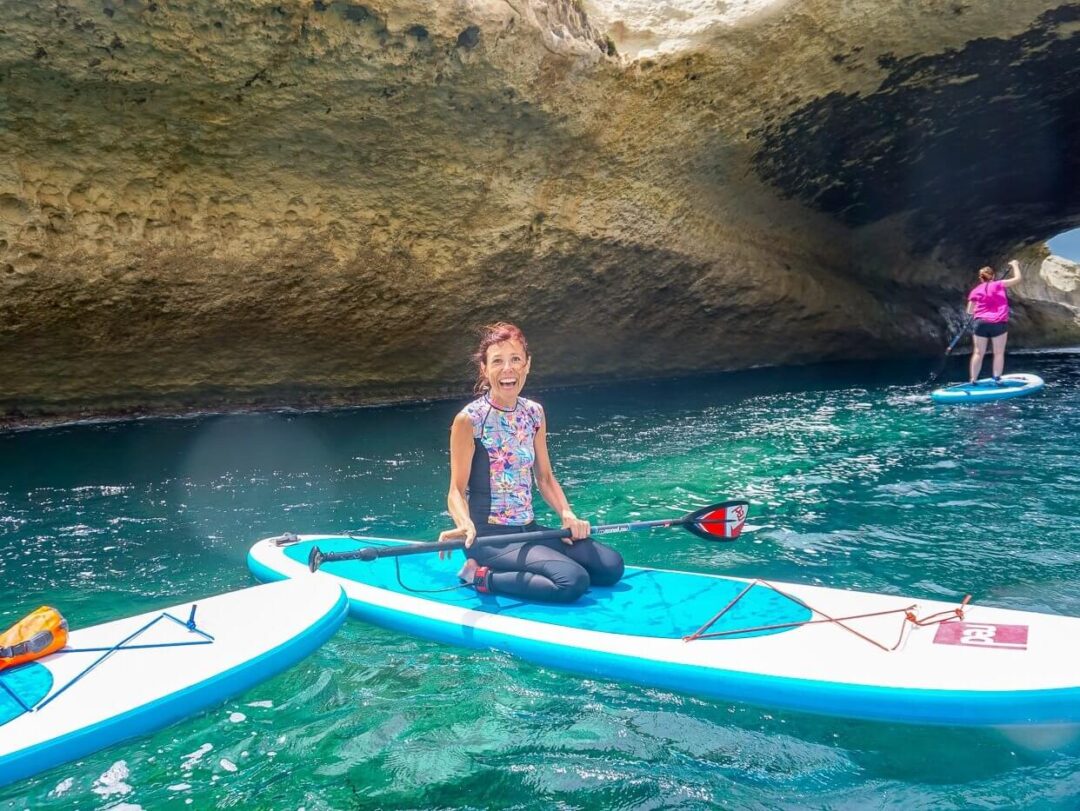 Woman paddleboarding on a stand-up paddleboard in a coastal sea cave, turquoise water in Sardinia