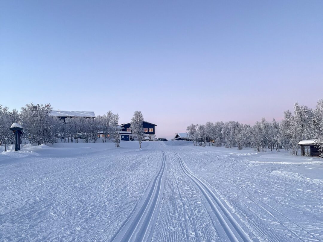 Cross-country ski trail through snowy countryside with tracks leading to a winter lodge and cabins