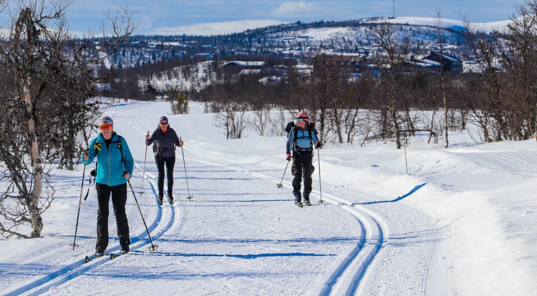 Women cross-country skiing on a snowy mountain trail with ski tracks in the background