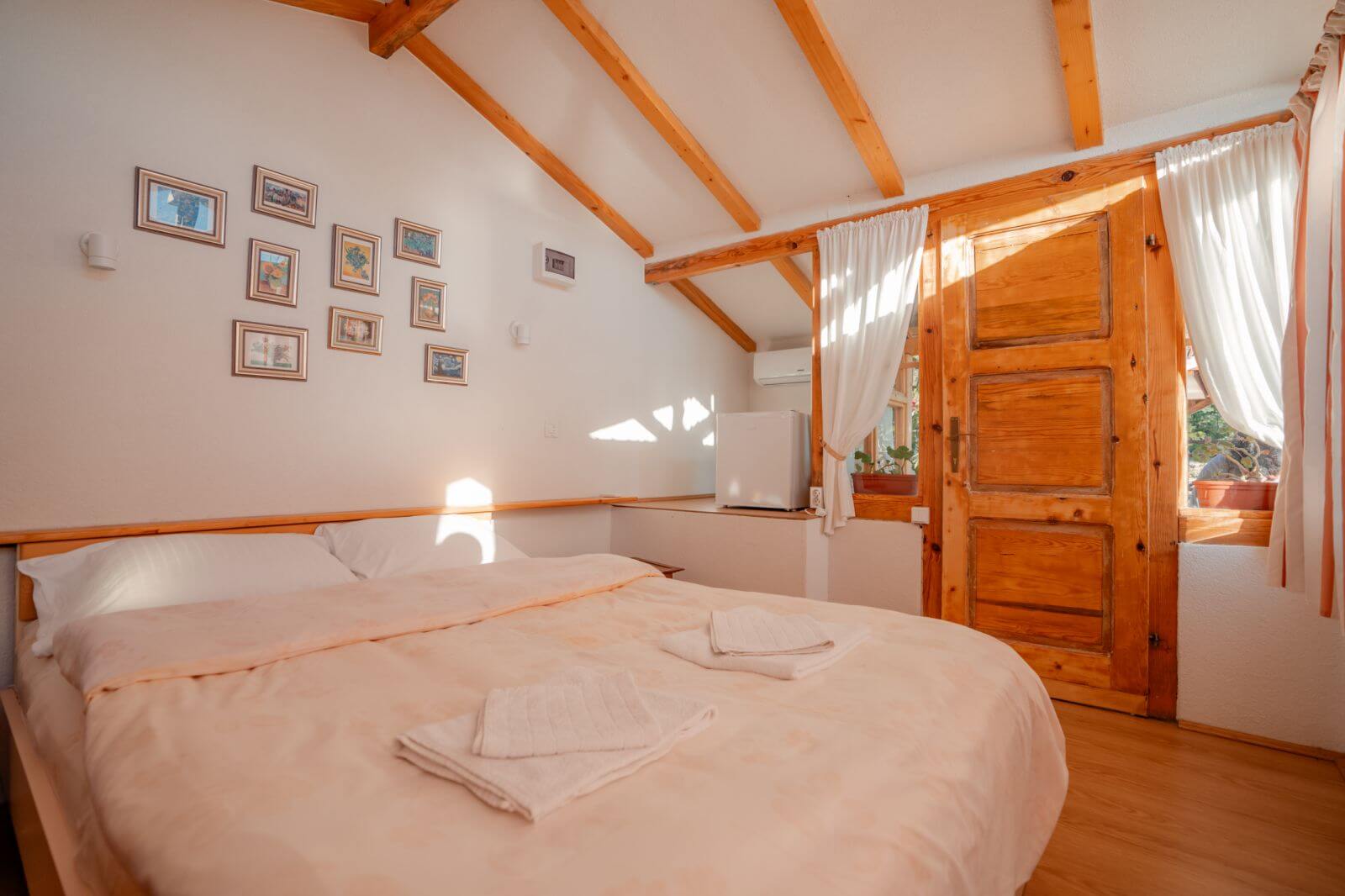 Wooden double bedroom interior with a neatly made bed and French windows.