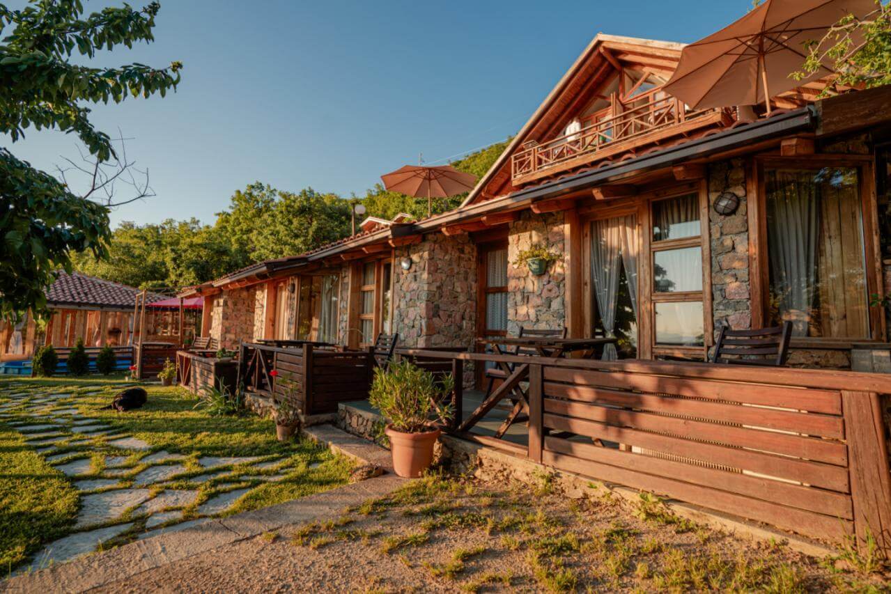 Rustic stone-and-wood cabins with patio seating and a garden walkway under a blue sky