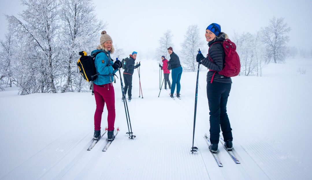 Women cross-country skiing on a snowy trail through winter forest, with ski poles and winter gear