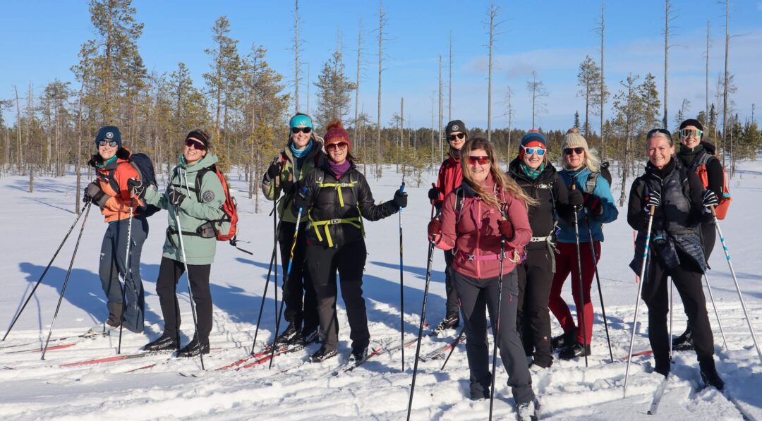 Women cross-country skiing on a snowy trail in a winter forest with poles and skis visible