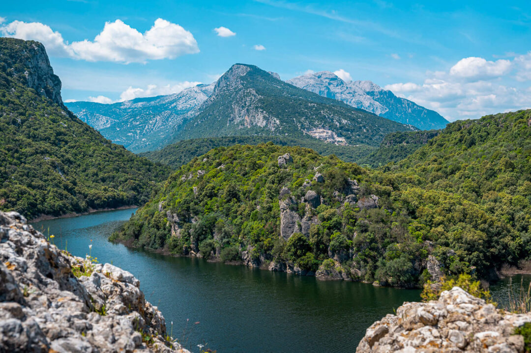 Turquoise river winding through forested mountains under a blue sky in East Sardinia