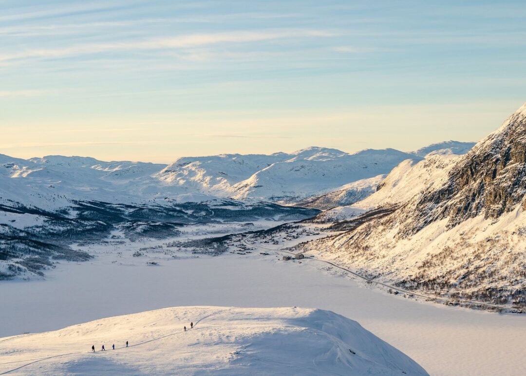 Snowy Norwegian mountains and ski slope overlooking a valley with tracks and skiers at sunset