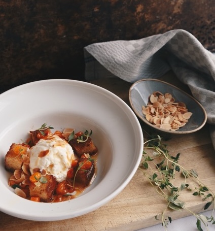 Warm winter stew with sour cream and herbs in a bowl, with chopped nuts beside it on a wooden table