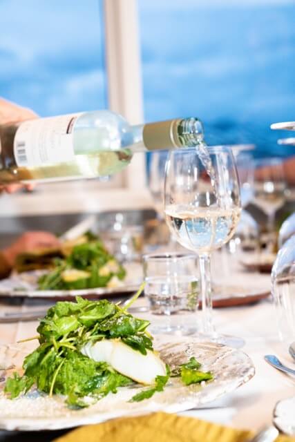 Wine bottle pouring into a glass on a dining table with plates of food and cutlery
