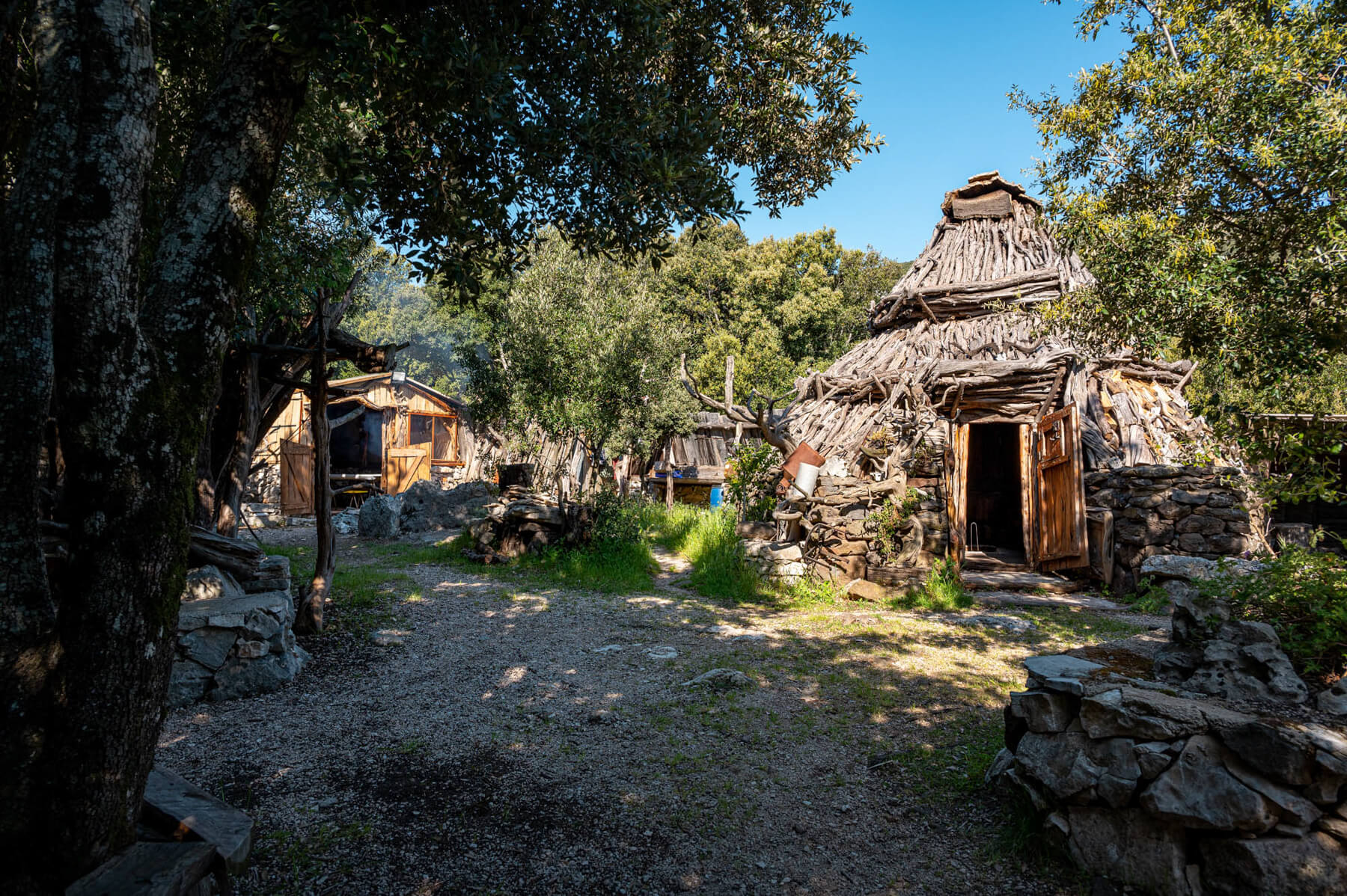 Hiking trail past rustic stone huts with thatched roofs among Mediterranean trees
