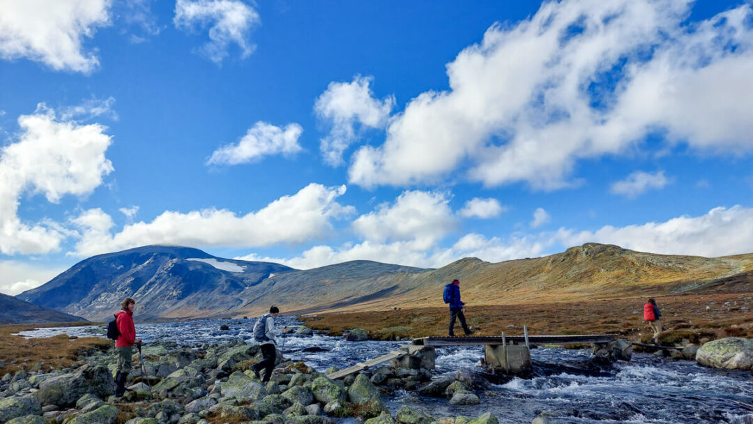 Women hiking along a rocky river with mountain views in Norway under a blue sky