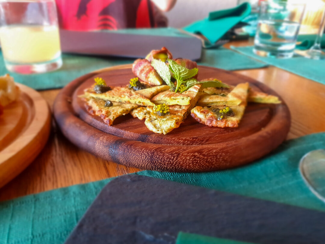 Pizza with herbs and vegetables on a wooden board on a table at an outdoor meal setting