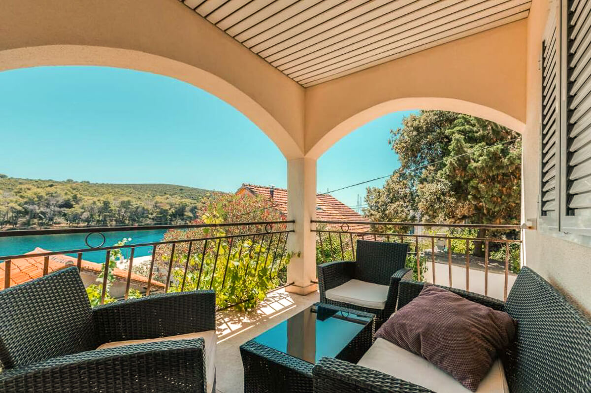 Balcony with outdoor seating overlooking a calm harbour and green hills