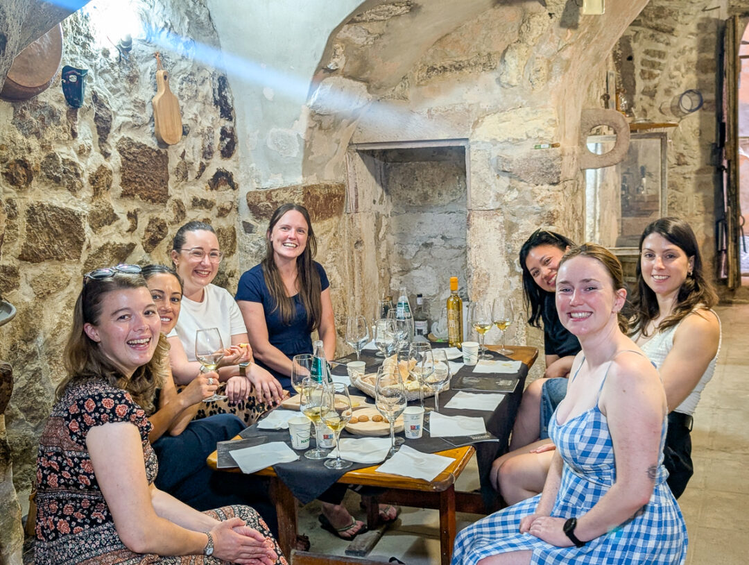 Women dining together in a rustic stone room with wine glasses, during a relaxing holiday in Sardinia