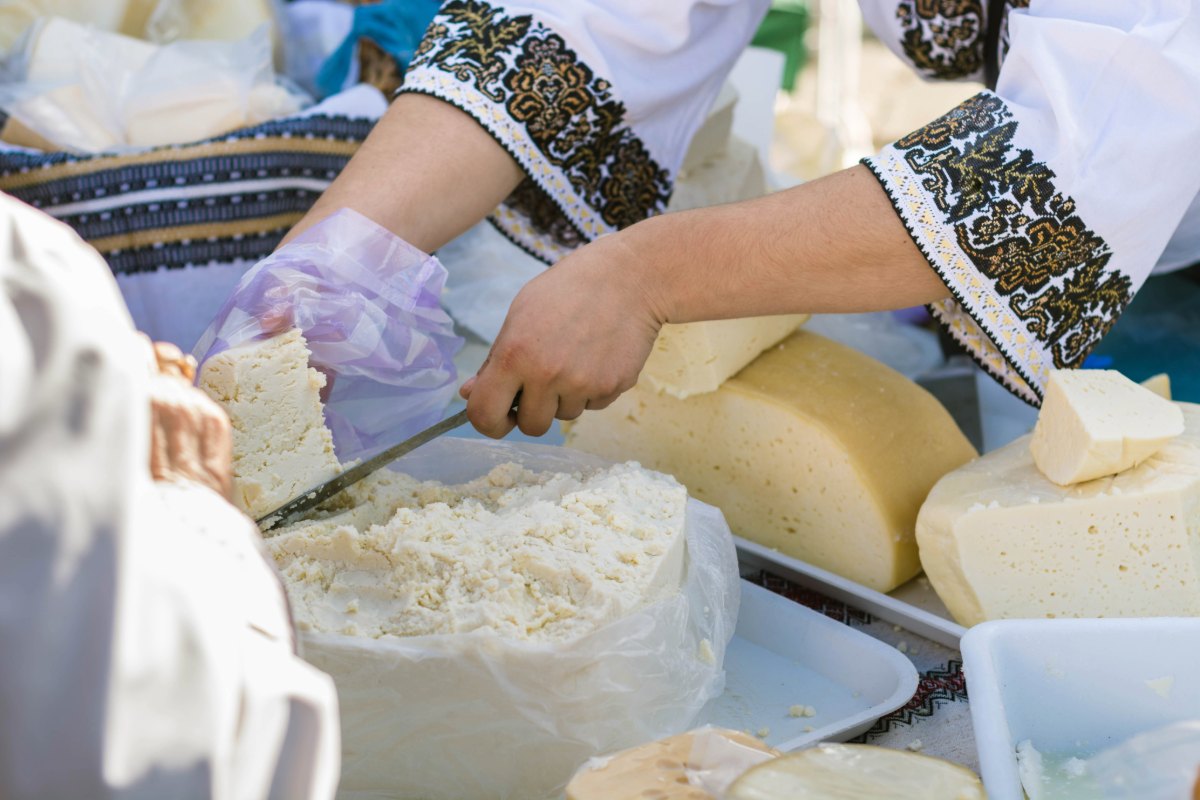 Woman preparing cheese, hands kneading and cutting cheese on trays outdoors in embroidered traditional clothing