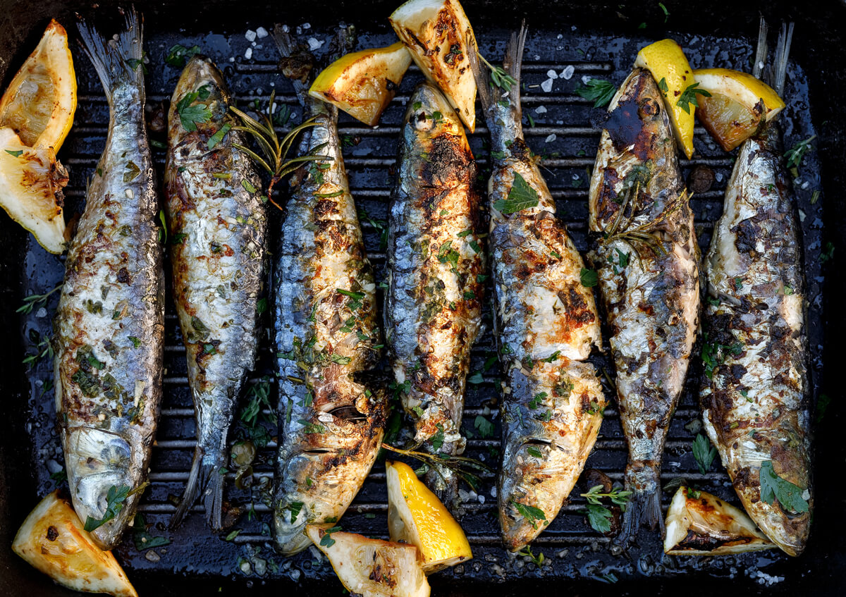 Grilled sardines on a barbecue tray with lemon wedges and herbs