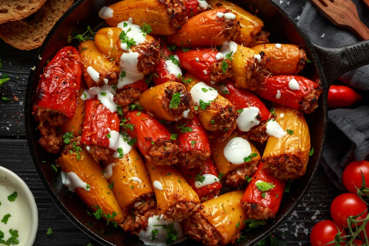 Roasted peppers and mixed vegetables with melted cheese in a skillet, with fresh herbs and tomatoes