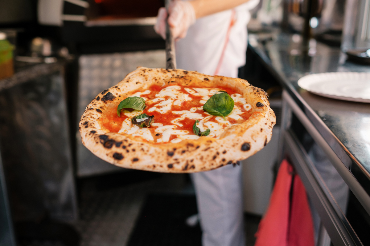 Wood-fired pizza with tomato sauce and fresh basil being cooked in a pizzeria kitchen