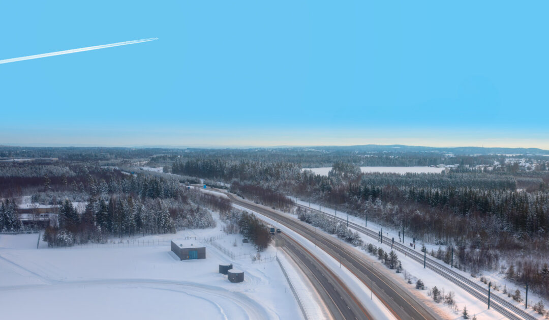 Aerial view of snowy Norwegian countryside with a road winding past forest and fields under a winter sky