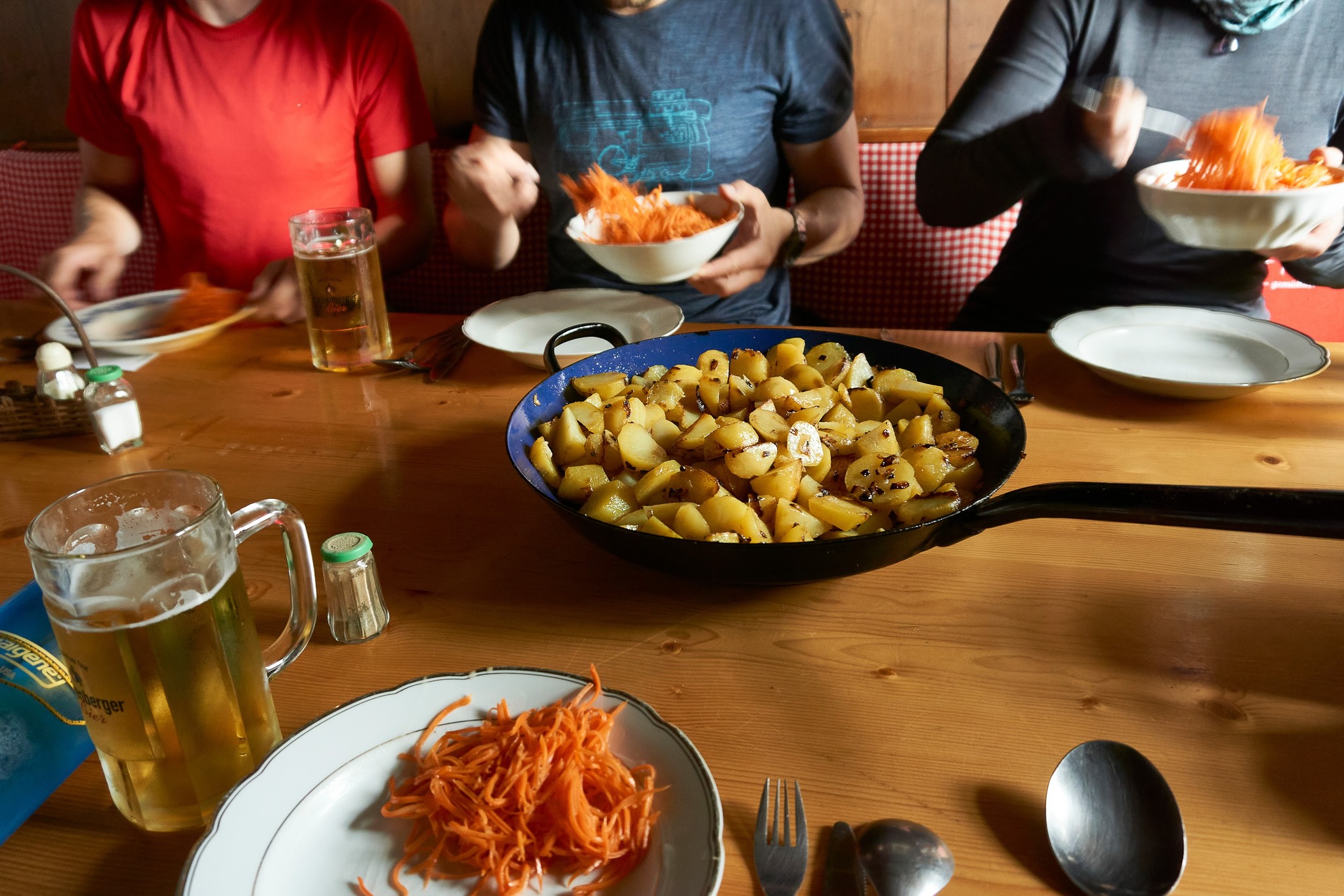 Women sharing a meal at a wooden table with bowls of pasta and vegetables