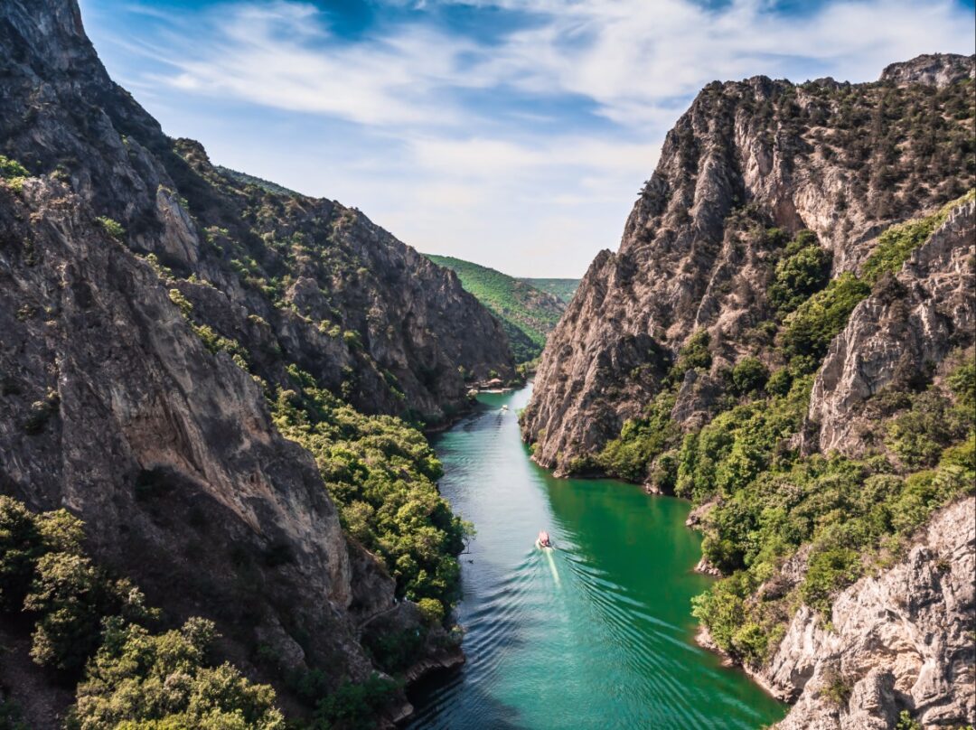 Boat on a calm river winding through steep mountain canyon with forests and rocky cliffs