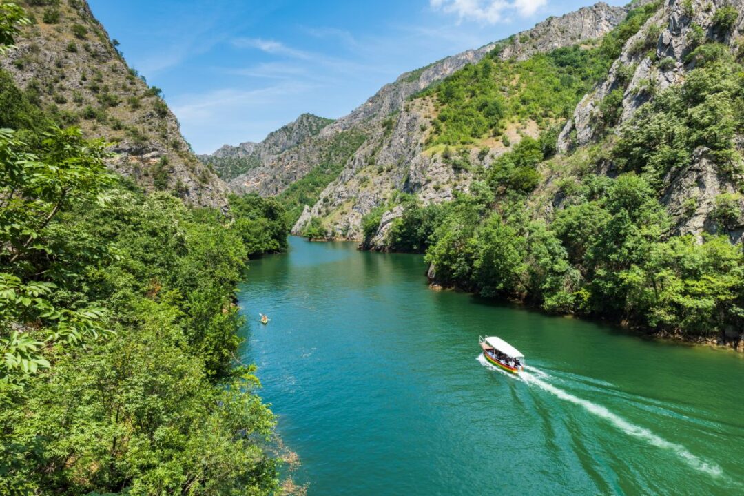 Boat on a turquoise river winding through a lush mountain valley and rocky cliffs