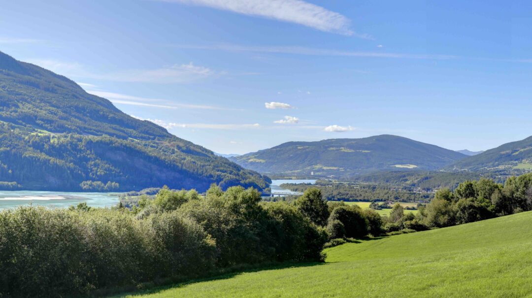 Scenic countryside valley with green fields, river and distant mountains under a blue sky